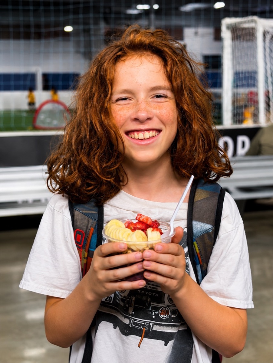 Smiling young guest holding a fresh Aura Açaí bowl at a Los Angeles sports event
